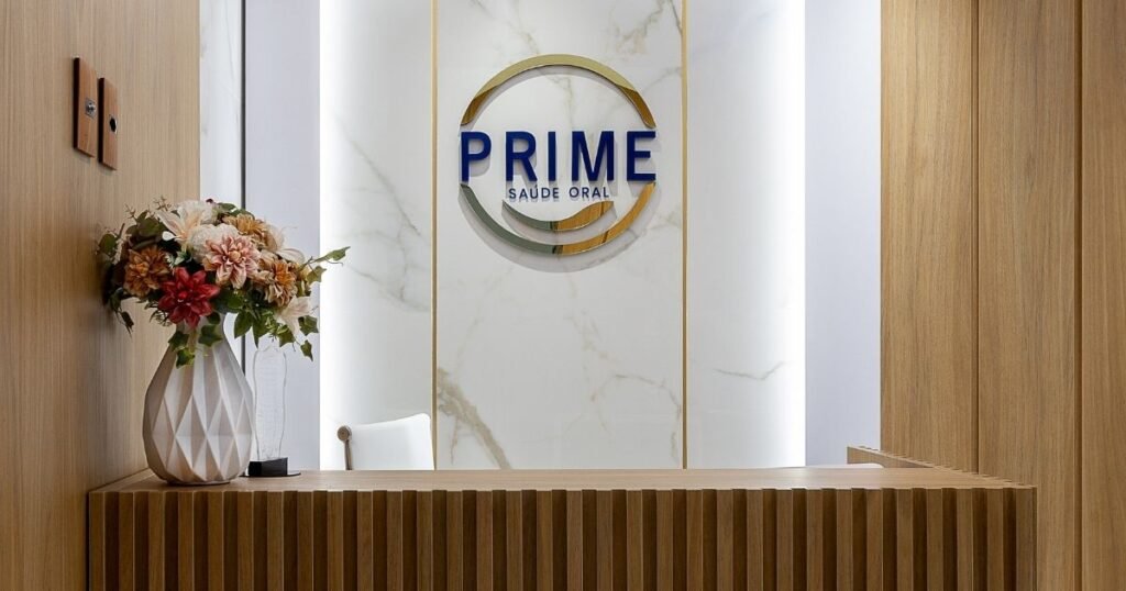 Recepção moderna da clínica Prime Saúde Oral em Alphaville, com balcão de madeira e logotipo em parede de mármore.