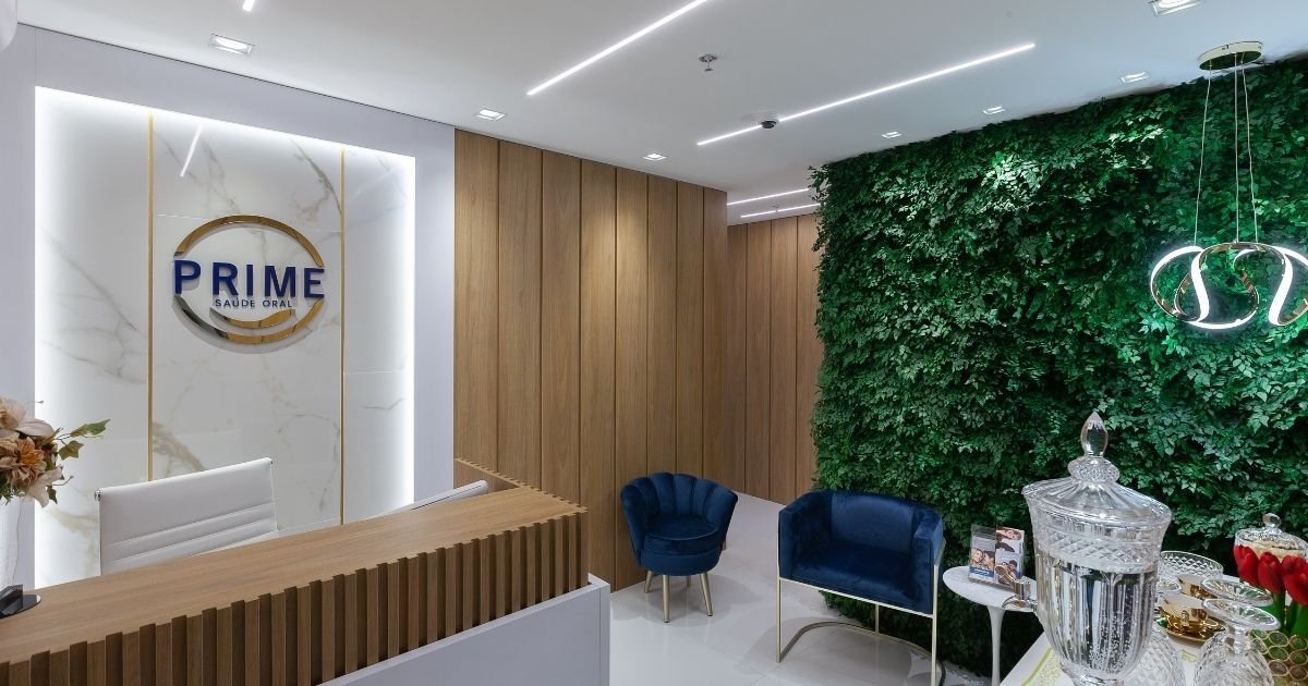Sala de espera confortável com jardim vertical (parede verde), poltronas de veludo azul e iluminação moderna na Prime Saúde Oral.