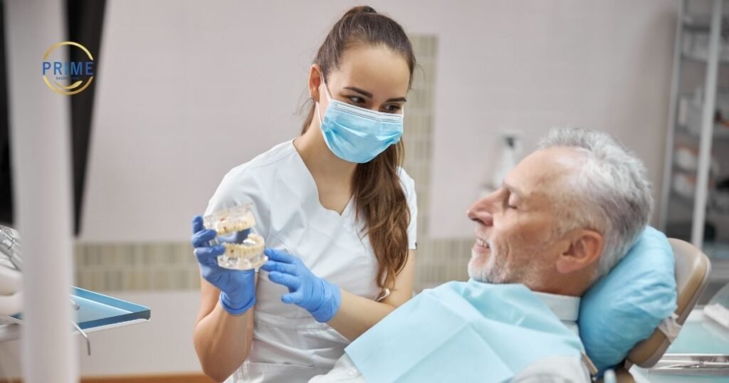 Dra. Vanessa Nani na Prime Saúde Oral em Alphaville, mostrando um modelo de arcada dentária para um paciente idoso durante consulta de avaliação.