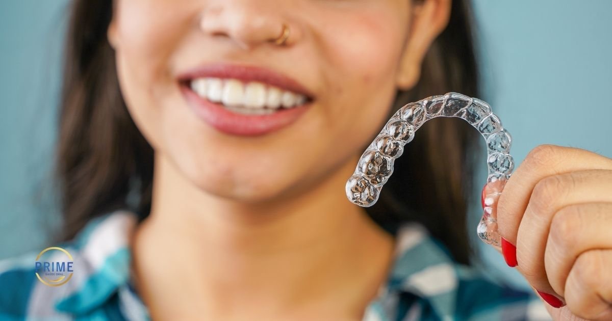 Jovem sorrindo segurando um alinhador transparente Invisalign próximo ao rosto, demonstrando que o aparelho é imperceptível.