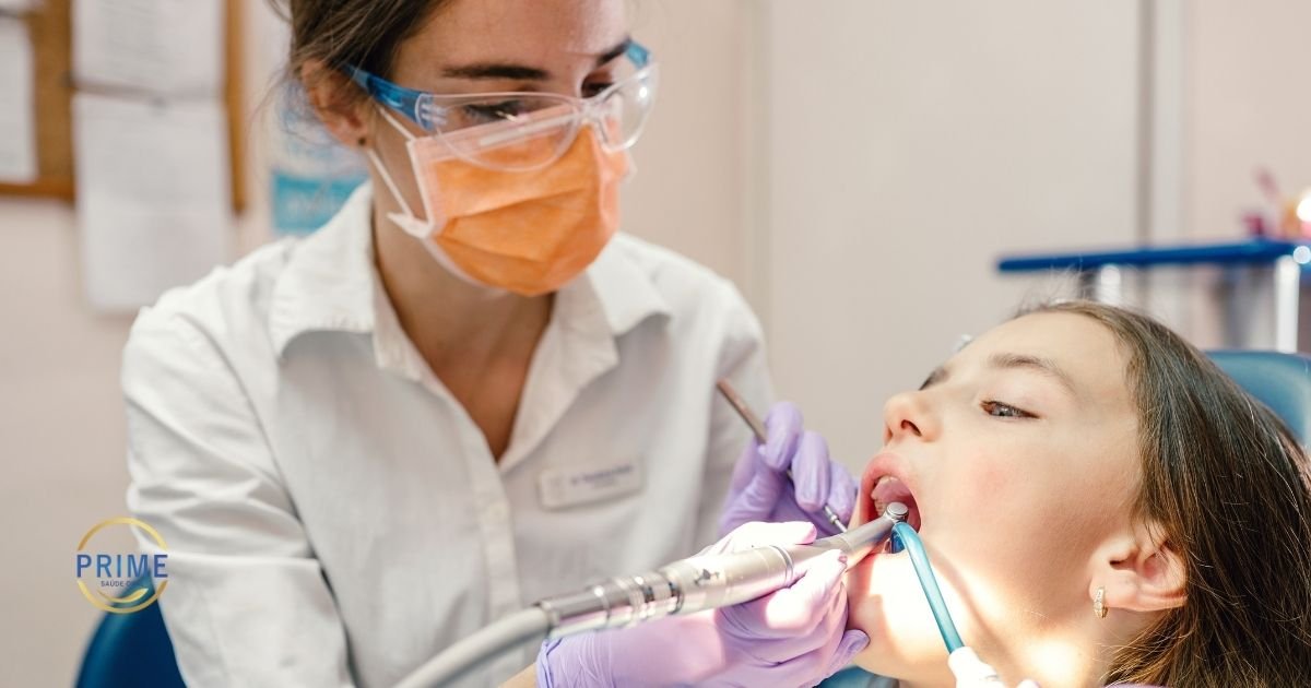 Dentista com máscara e óculos de proteção realizando procedimento odontológico em paciente jovem reclinada na cadeira, com logo da Prime Saúde Oral