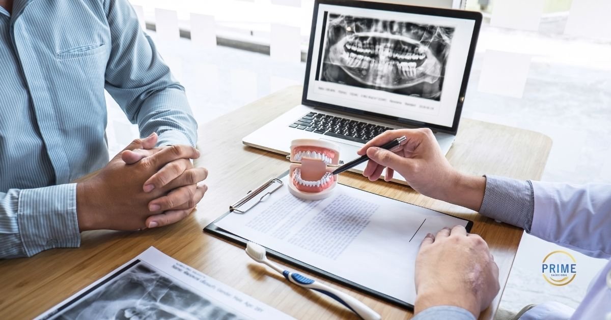 entista explicando plano de tratamento para paciente usando modelo de arcada dentária, com radiografia panorâmica digital exibida no notebook ao fundo, com logo da Prime Saúde Oral