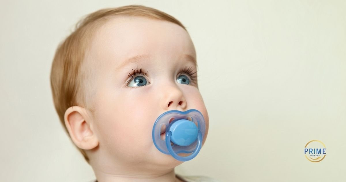 Bebê de olhos azuis com chupeta azul na boca em fundo claro, com logo da Prime Saúde Oral