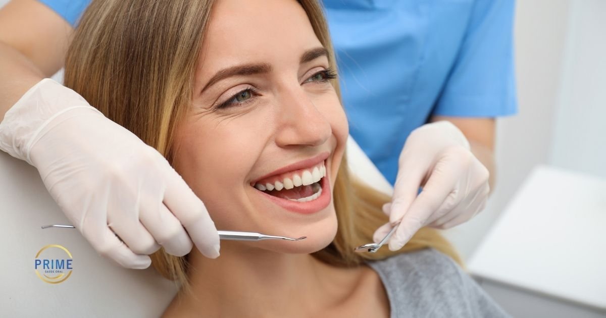 alternativoPaciente jovem sorrindo durante atendimento odontológico com dentista de luvas brancas e uniforme azul utilizando instrumentos de exame, com logo da Prime Saúde Oral