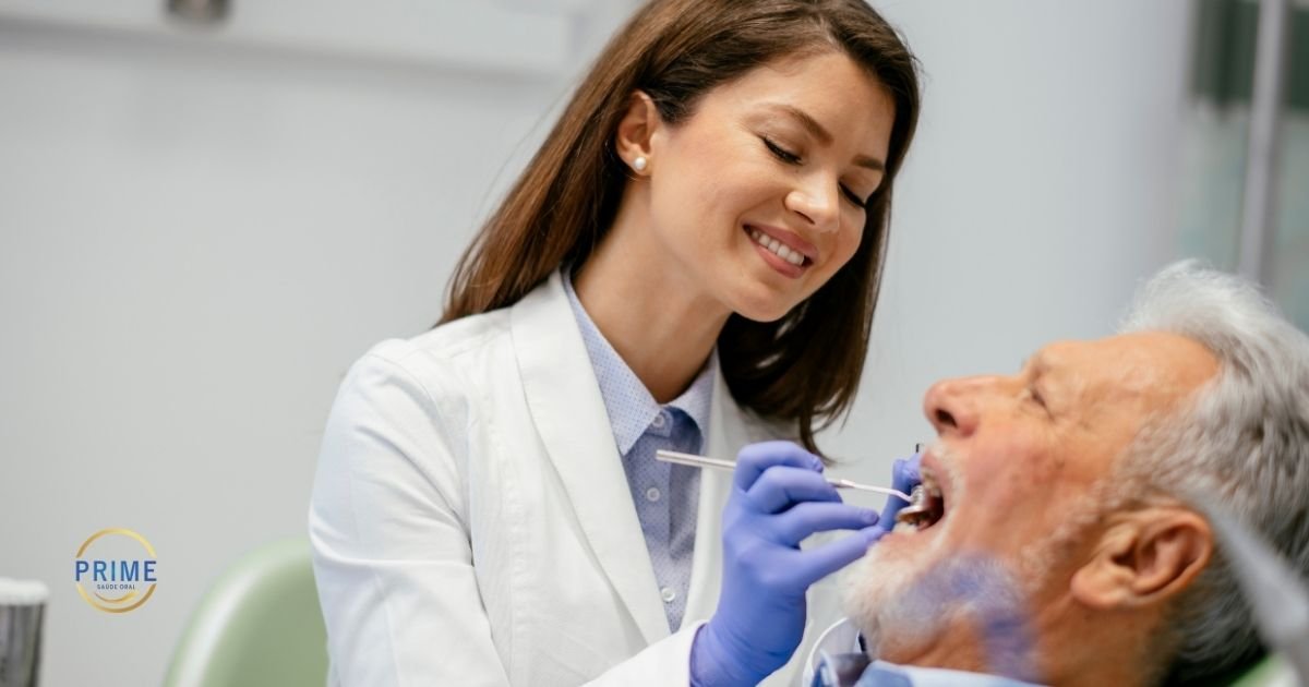 Dentista jovem sorrindo enquanto examina paciente idoso de cabelos brancos reclinado na cadeira odontológica, com instrumentos de exame, com logo da Prime Saúde Oral