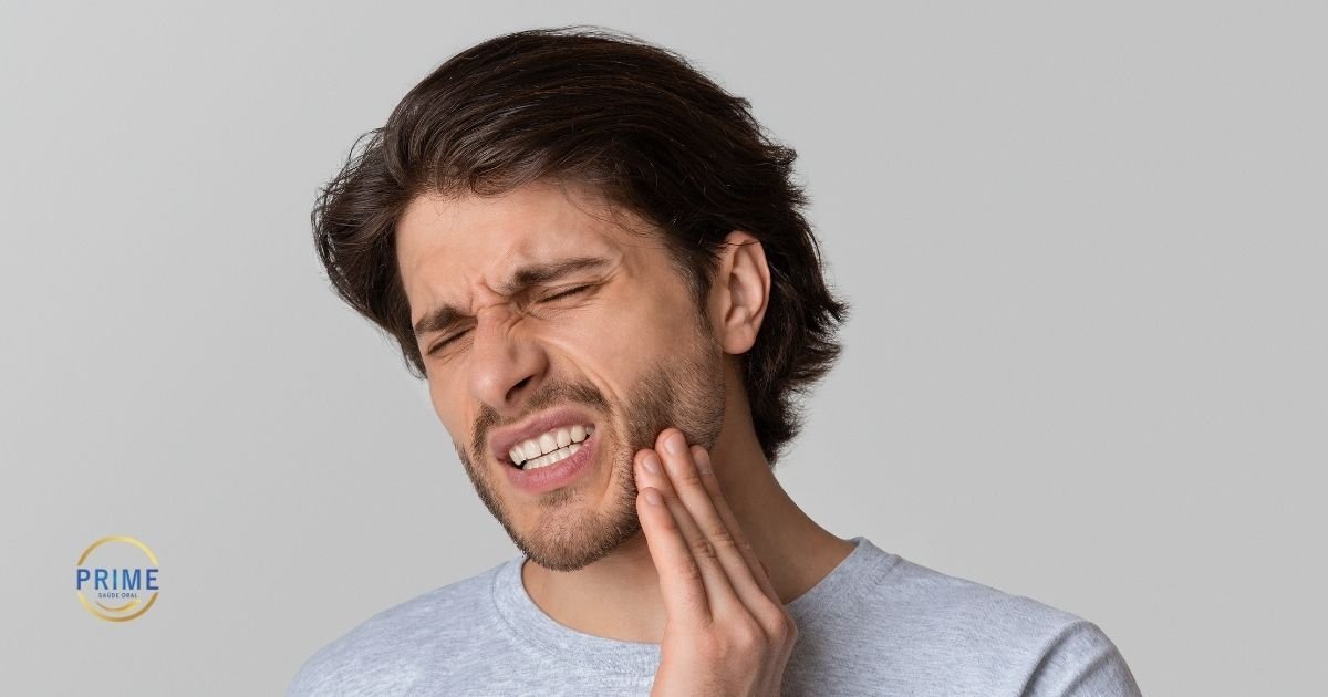 Homem jovem com expressão de dor intensa segurando a região da mandíbula com a mão, ilustrando dor de dente, com logo da Prime Saúde Oral